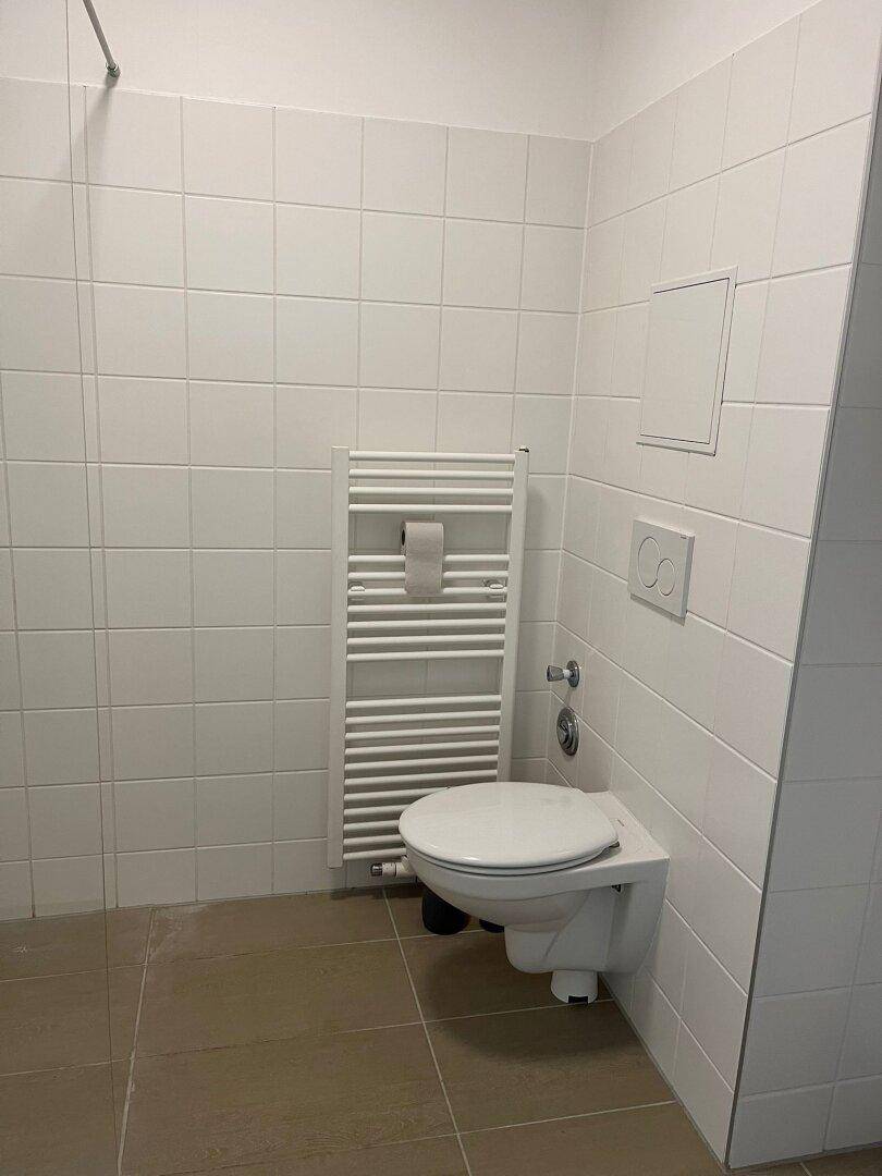 Helles Badezimmer mit weißen Fliesen, Wand-WC und beheiztem Handtuchhalter.