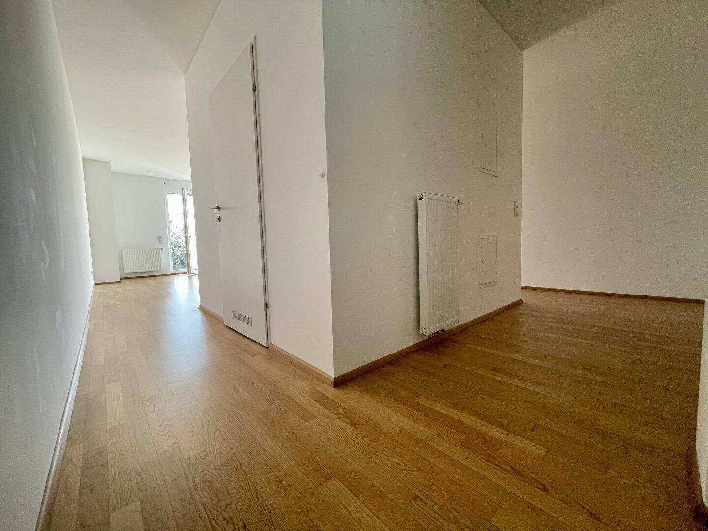 Heller Flur mit Holzboden und weißen Wänden, der zu weiteren Räumen führt.