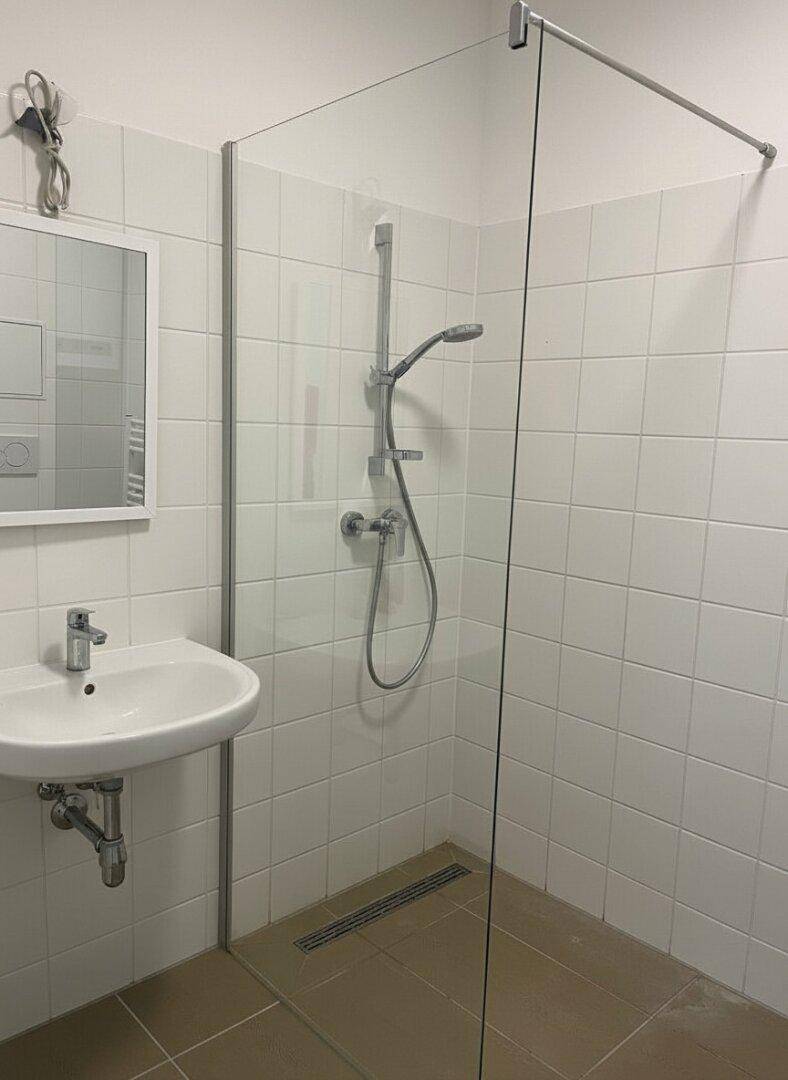 Modernes Badezimmer mit ebenerdiger Dusche, Waschbecken und Spiegel.