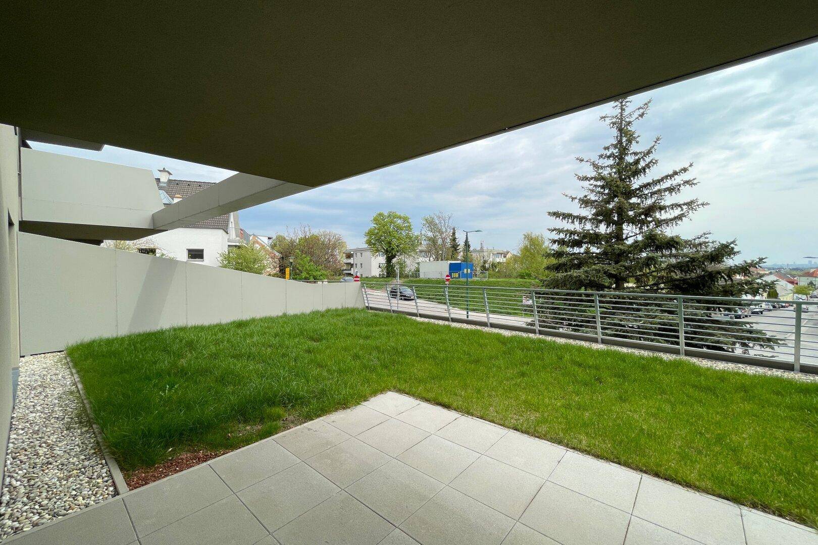 Gepflegter Gartenbereich mit Rasen und gepflasterter Terrasse vor dem modernen Wohngebäude.