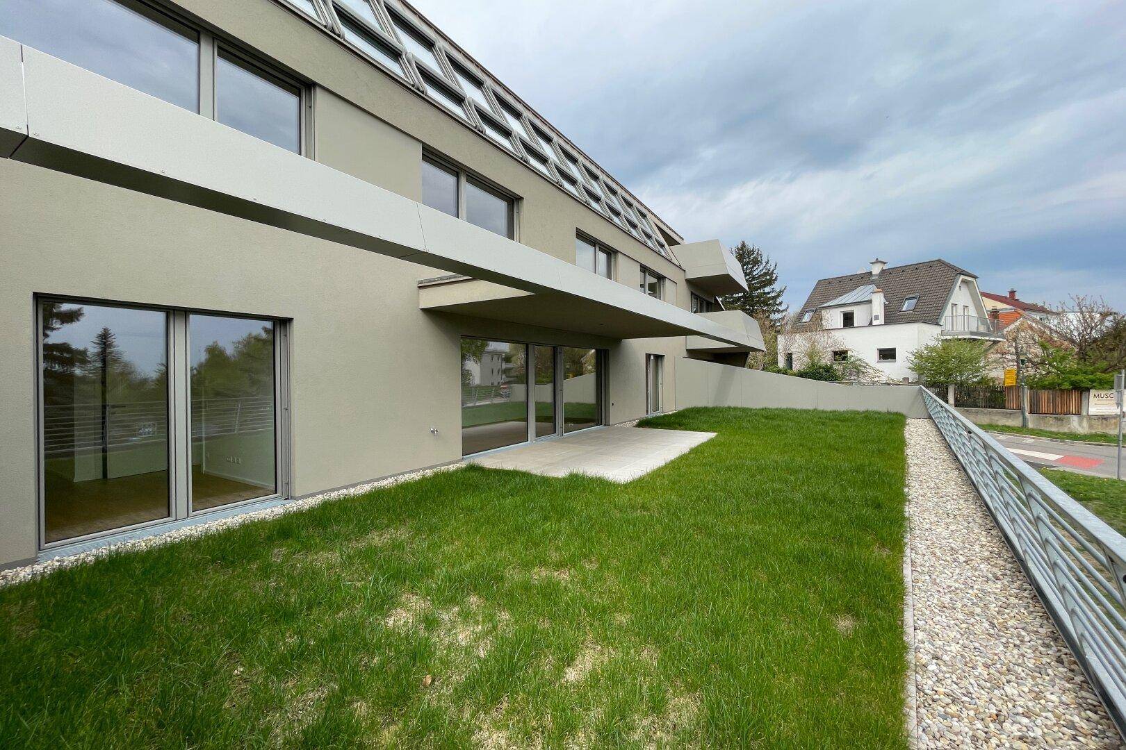 Moderne Gebäudefassade mit großen Fenstern und einer gepflegten Rasenfläche im Erdgeschoss.