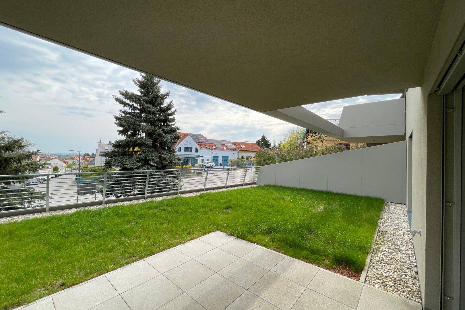Grüne Rasenfläche mit kleiner Terrasse und Blick auf die umliegende Wohngegend.