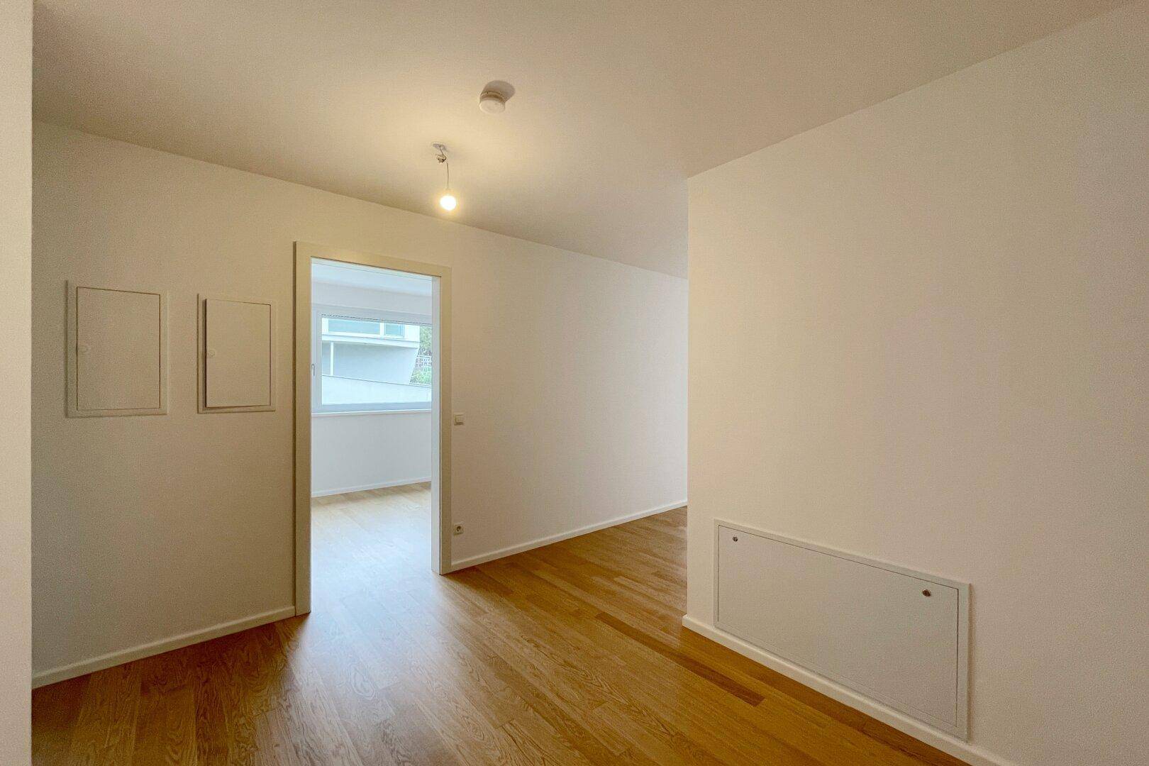 Geräumiger Flurbereich mit Holzboden und Zugang zu einem hellen Zimmer mit Fenster.