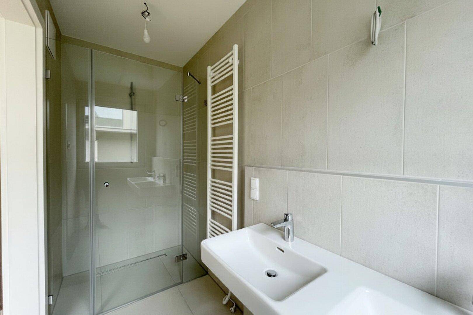 Modernes Badezimmer mit beigefarbenen Fliesen, ebenerdiger Dusche und beheiztem Handtuchhalter.