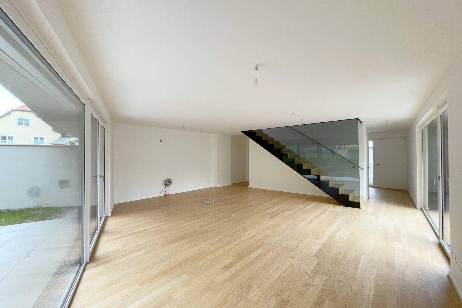 Geräumiger Wohnbereich mit Holzparkett, viel Tageslicht und moderner Treppe.