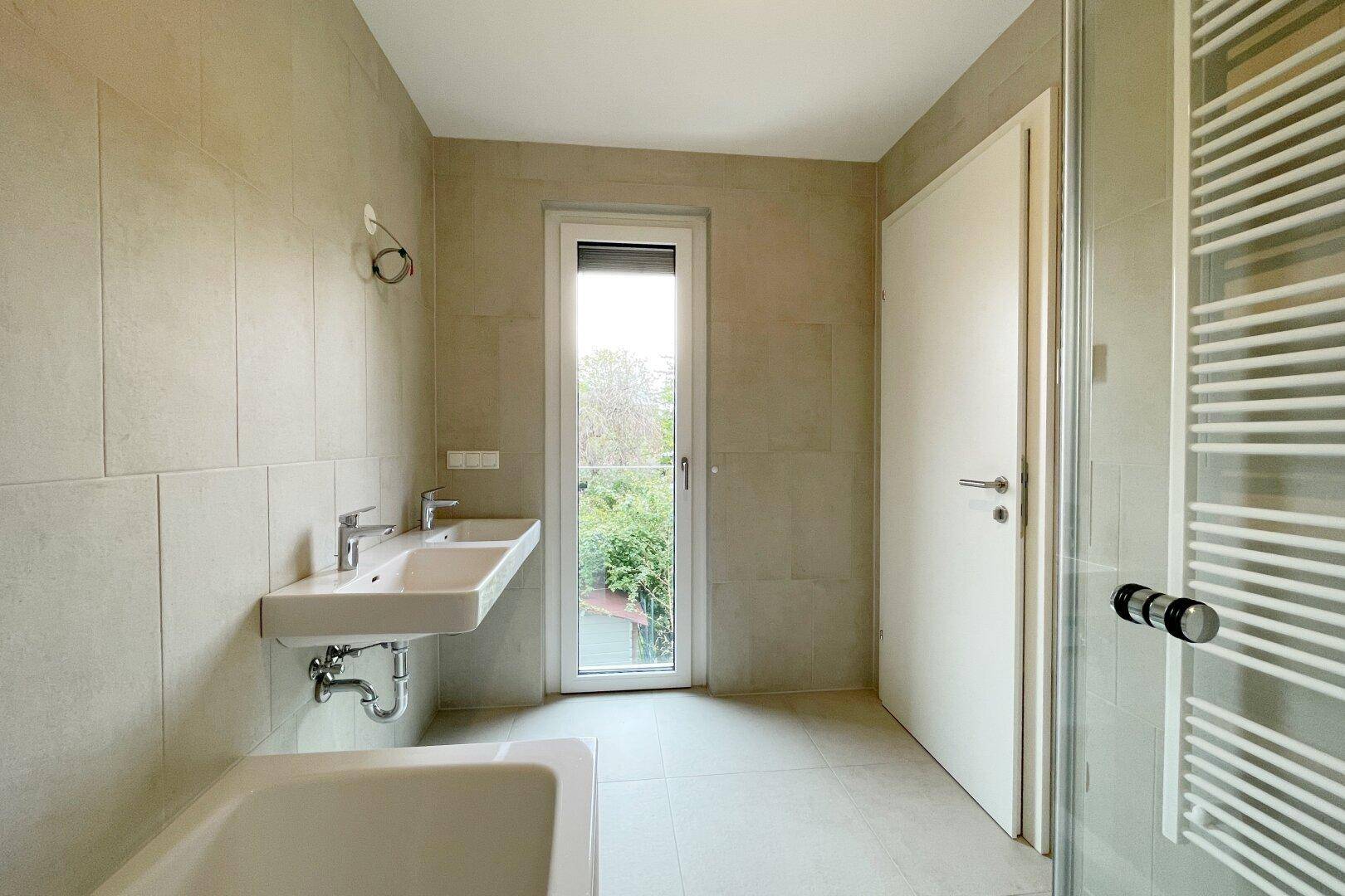 Modernes Badezimmer mit Doppelwaschbecken, Dusche und Fenster.