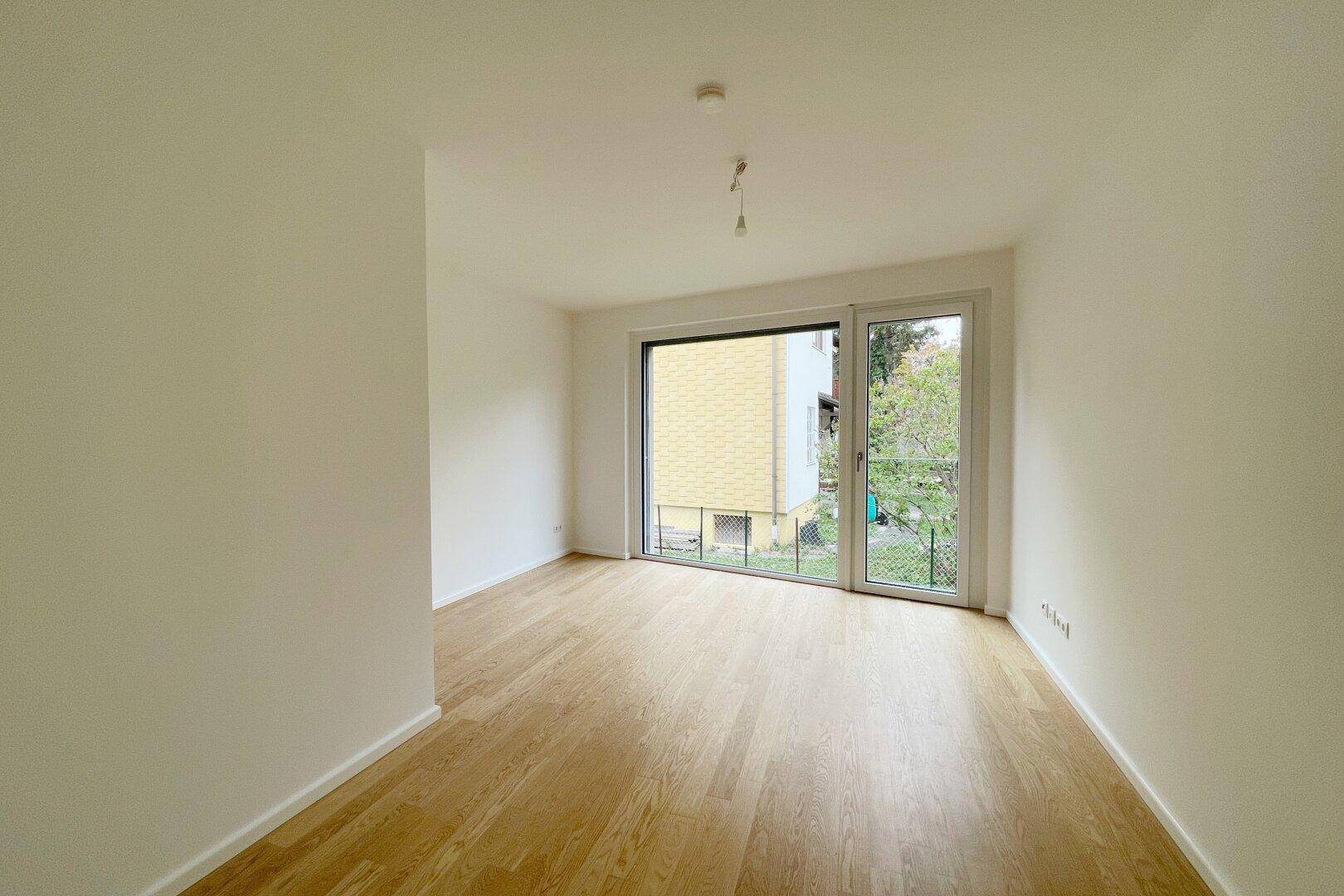 Geräumiges Zimmer mit Parkettboden und Fenster zum grünen Außenbereich.