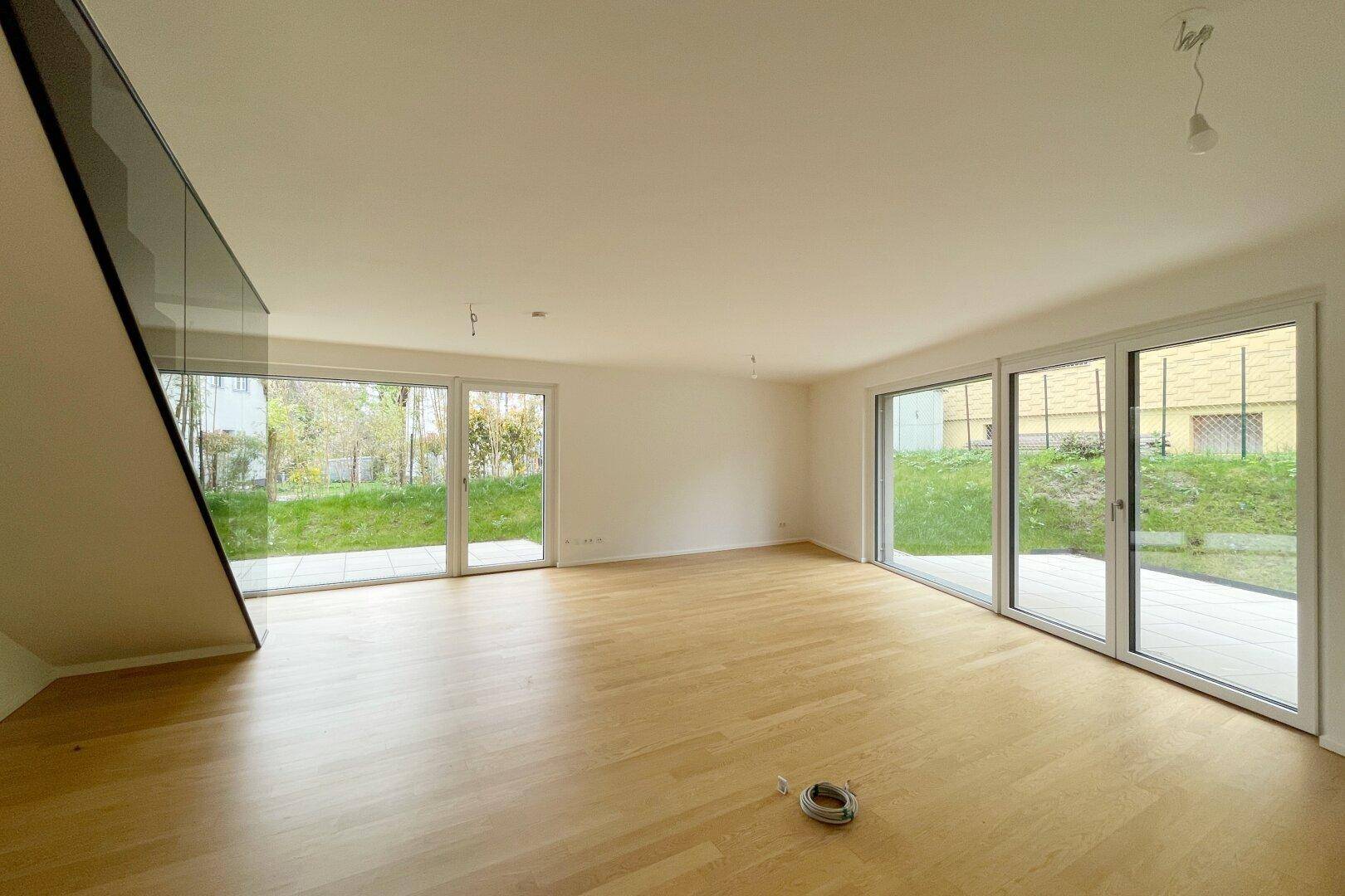 Heller, leerer Wohnbereich mit großen Fenstern und Zugang zur Terrasse.
