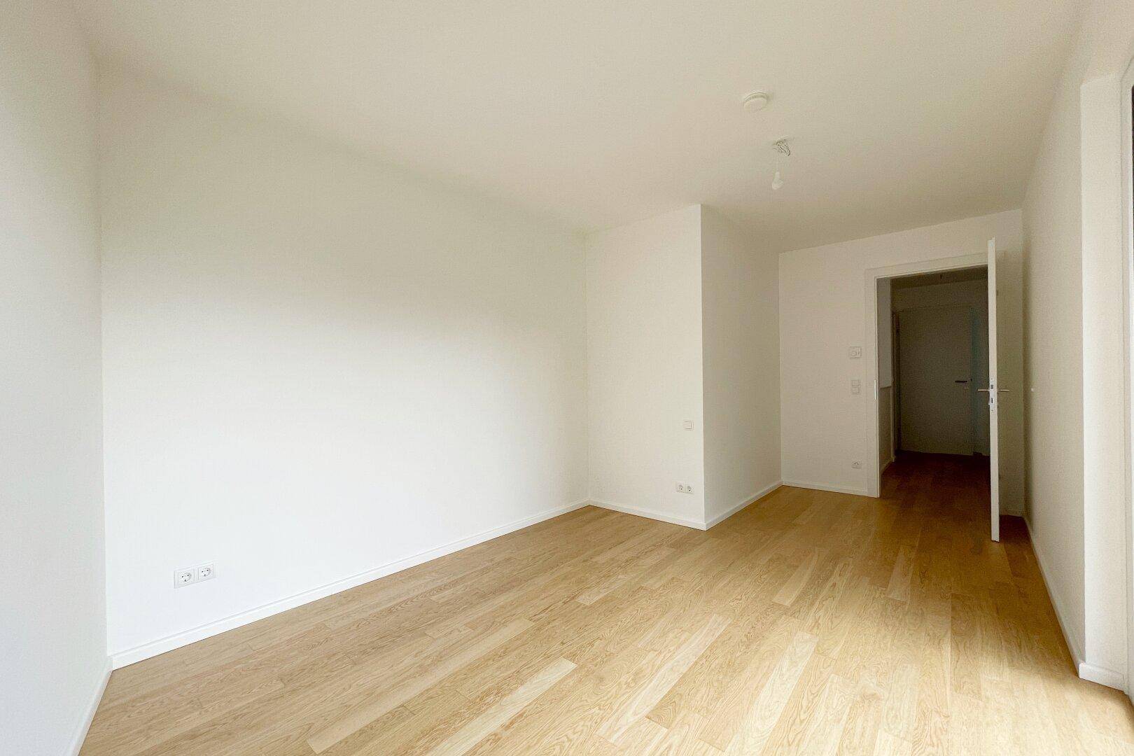 Leeres Zimmer mit hellem Parkettboden und weiß gestrichenen Wänden.