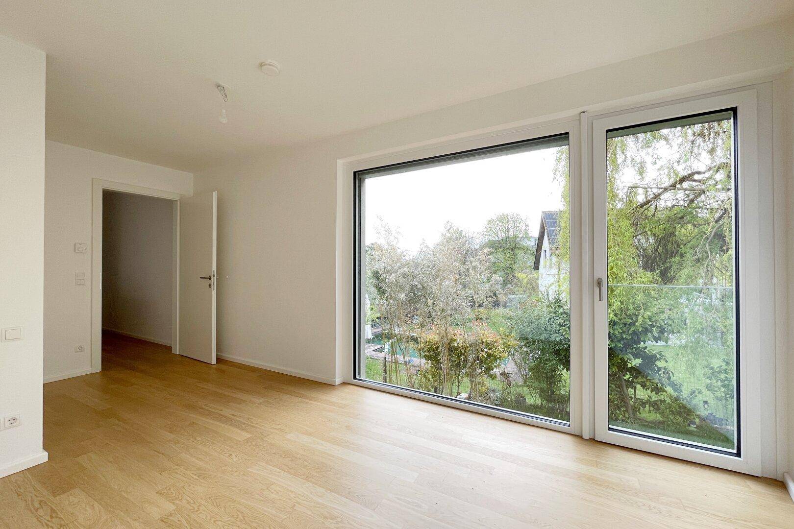 Helles Schlafzimmer mit Parkettboden und französischem Balkon mit Grünblick.