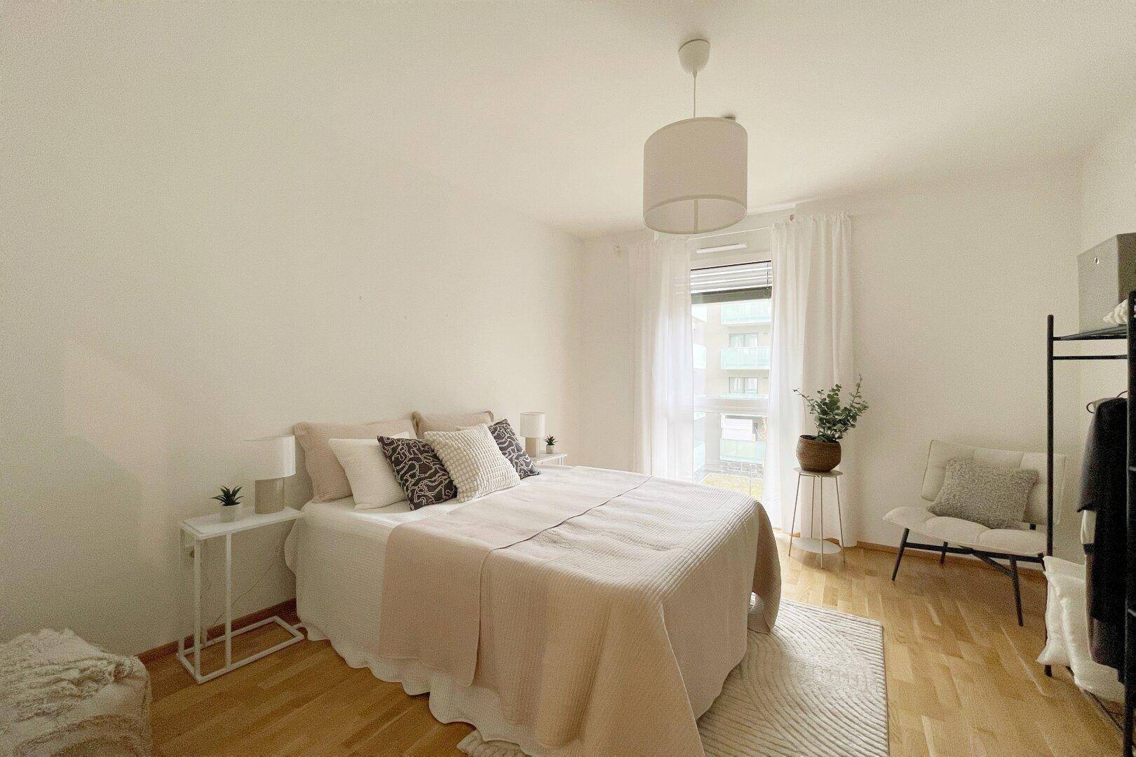 Gemütliches Schlafzimmer mit hellem Parkettboden, großem Fenster und moderner Einrichtung.