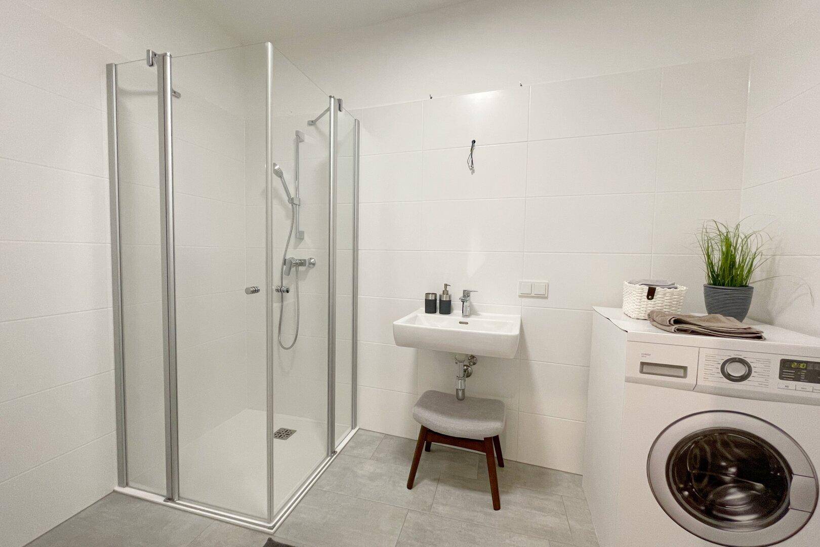 Modernes Badezimmer mit weiß gefliesten Wänden, Duschkabine und Waschmaschine.