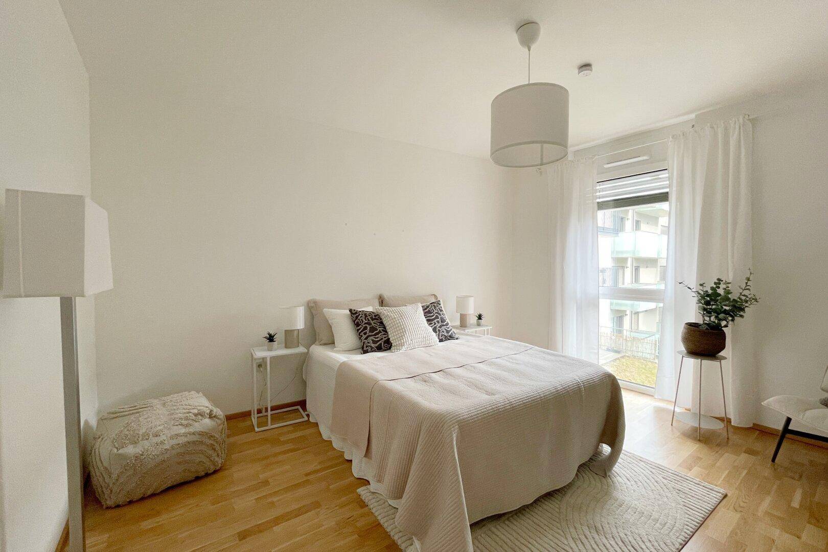 Helles Schlafzimmer mit Holzboden, großem Fenster und schlichter, moderner Einrichtung.