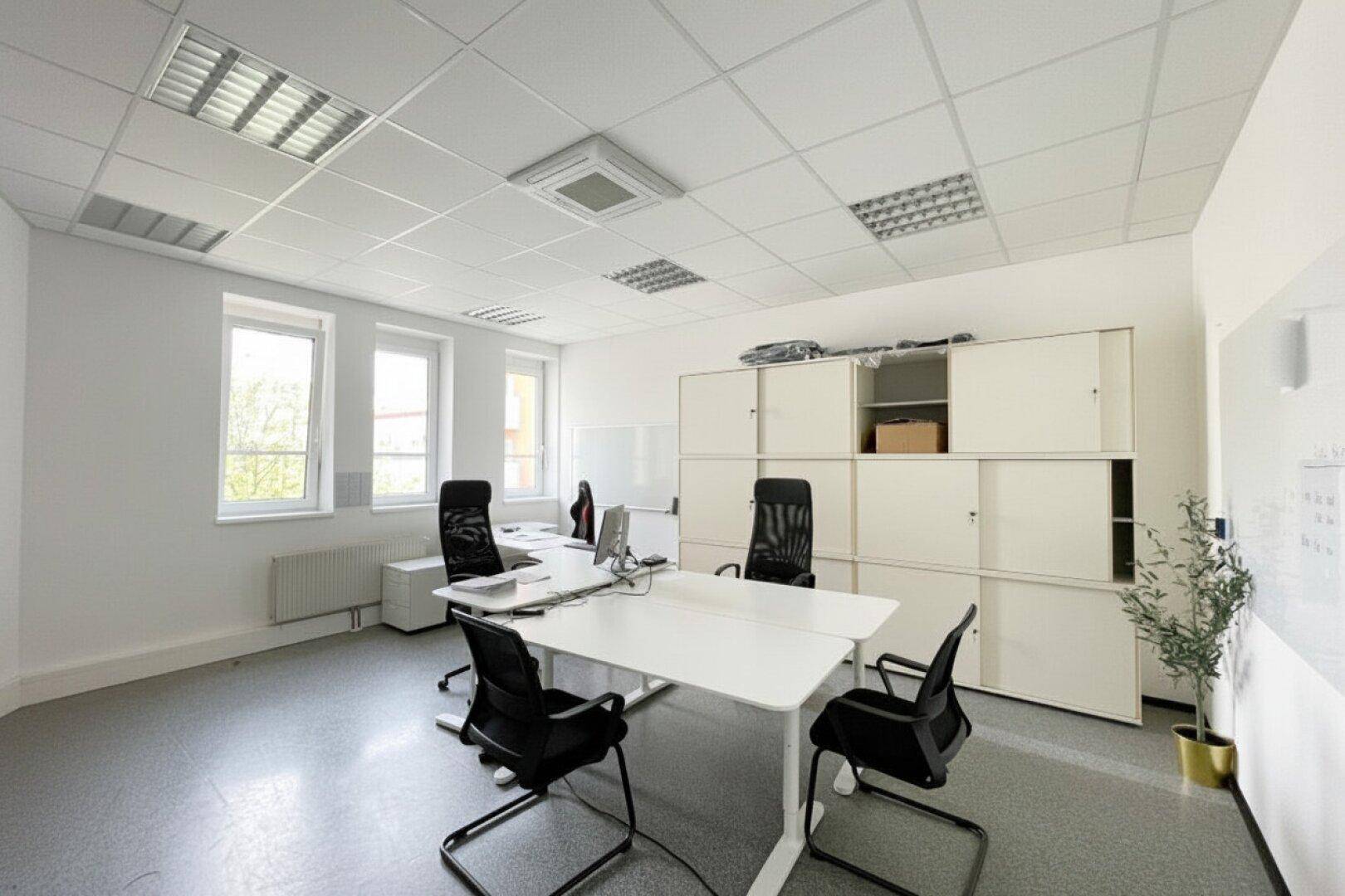 Modernes Büro mit mehreren Arbeitsplätzen, großen Fenstern und praktischen Lagerschränken.