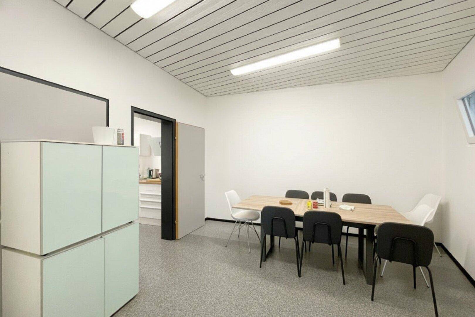 Besprechungsraum mit schräger Decke, Holztisch und modernen Stühlen, ideal für Teamtreffen.