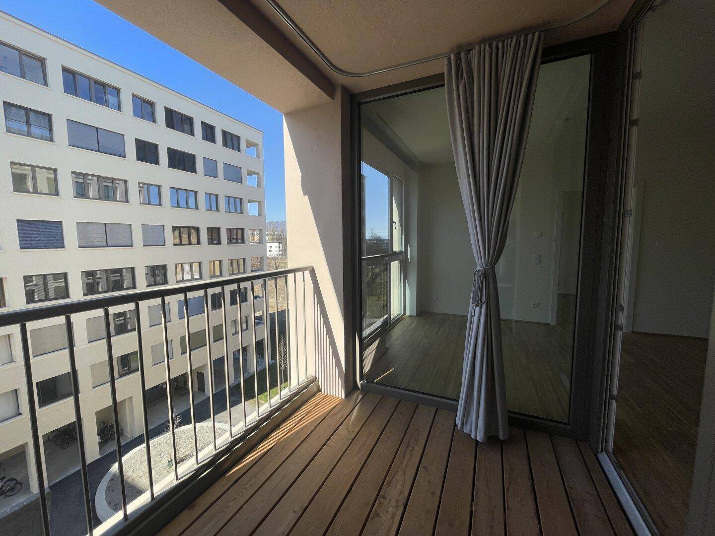 Sonniger Balkon mit Holzboden und Blick auf die umliegenden Gebäude.
