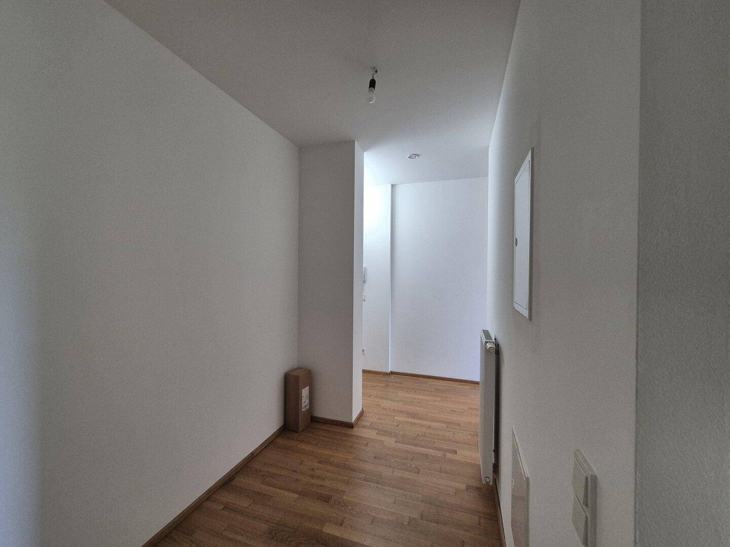 Langer, heller Flur mit Holzparkettboden und weiß gestrichenen Wänden, gut gepflegt.
