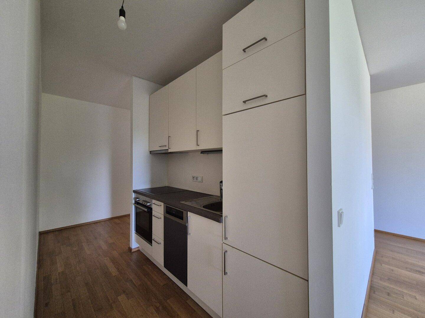 Kompakte Küchenzeile mit weißen Schränken, integriertem Backofen und dunkler Arbeitsplatte.