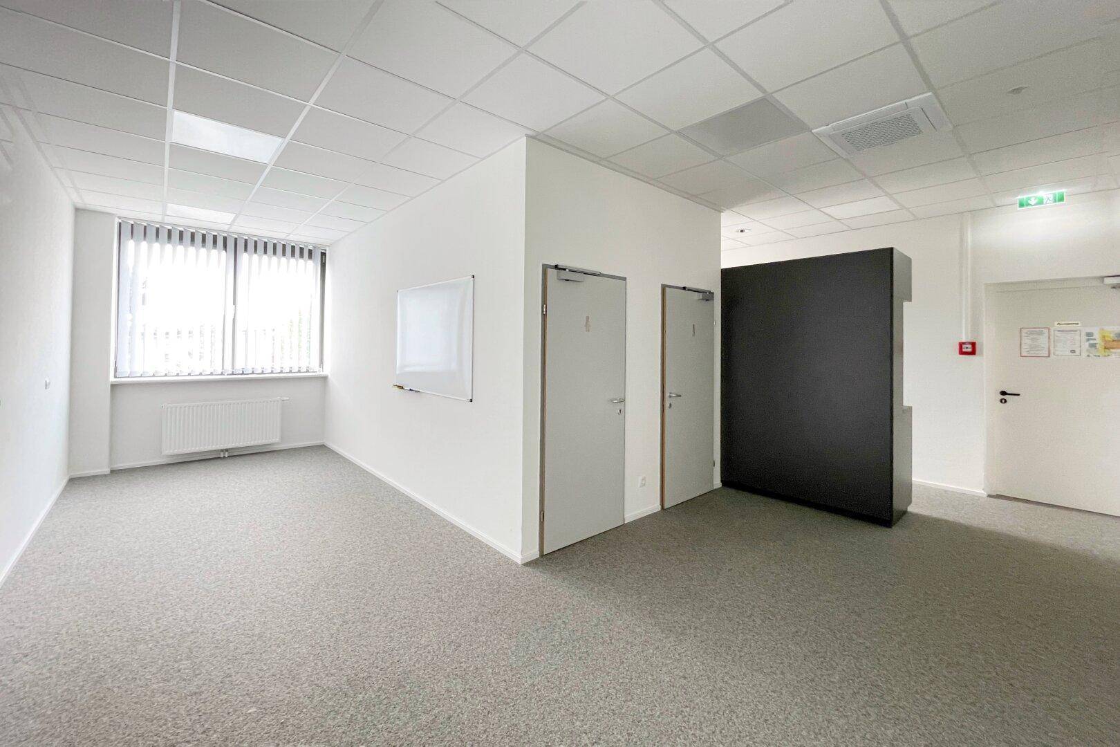 Bürobereich mit Teppichboden, Fenstern mit Jalousien und mehreren Türen zu angrenzenden Räumen.