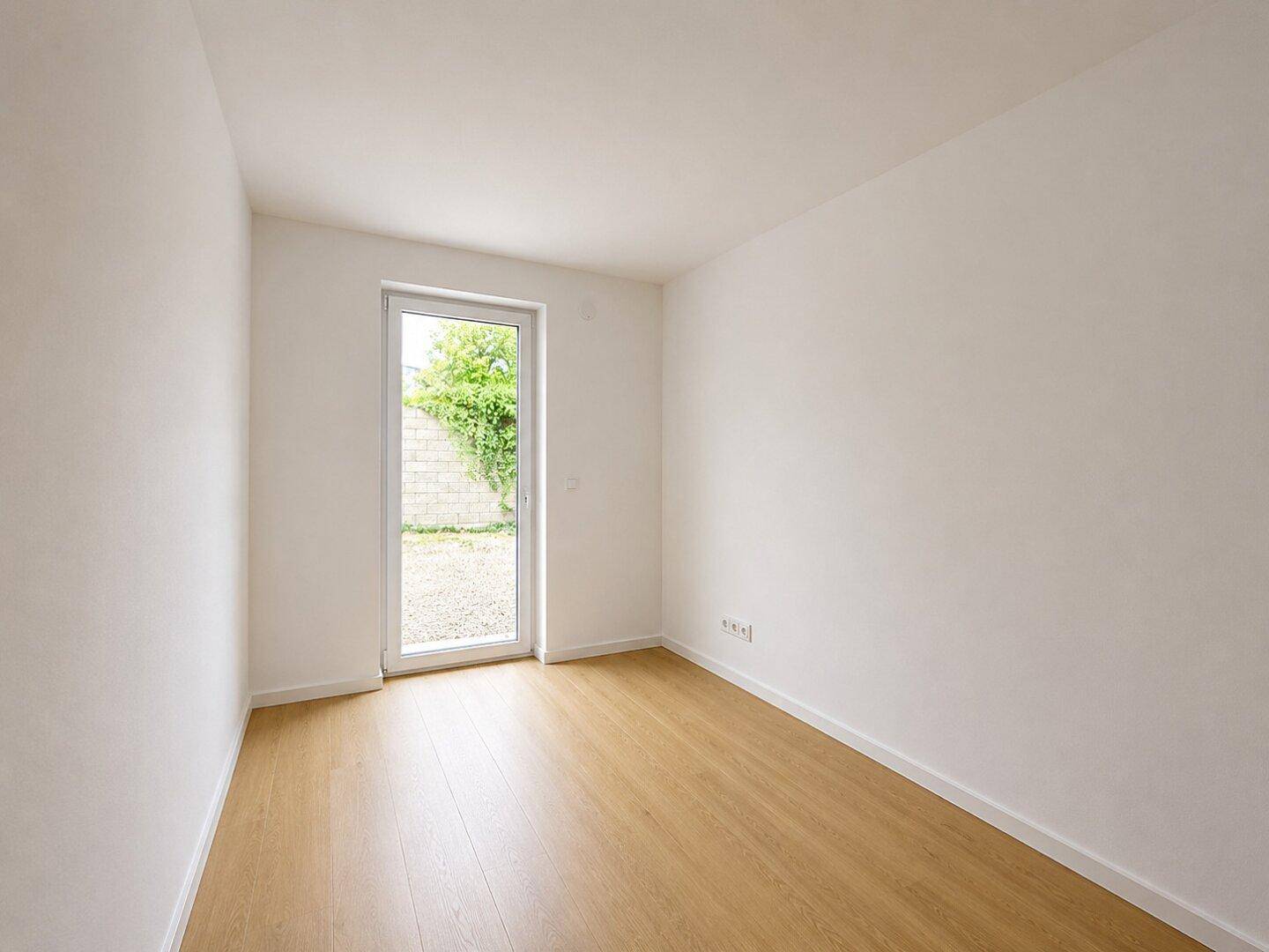 Leeres Zimmer mit Laminatboden und direktem Zugang zu einem kleinen Außenbereich.