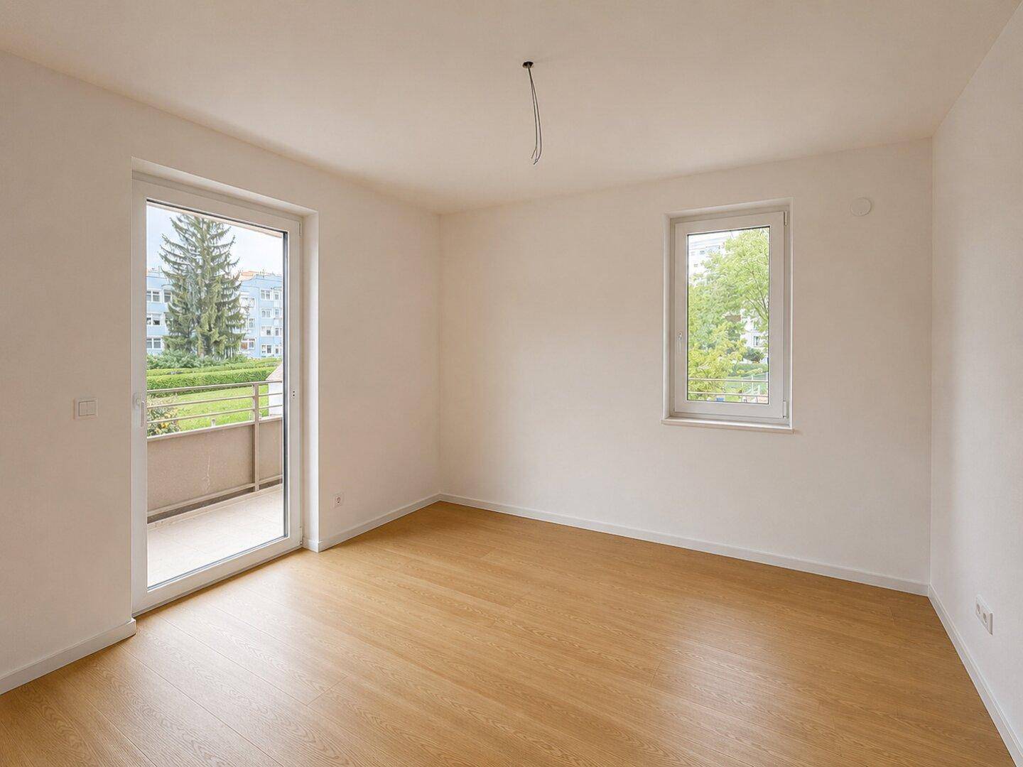 Geräumiges, leeres Zimmer mit Laminatboden, Balkonzugang und zusätzlichem Fenster.