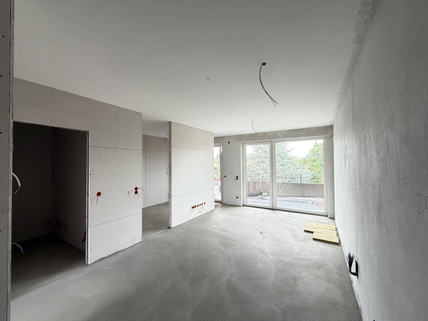 Rohbau eines Raumes mit Betonboden und großen Fenstern, bereit für den Ausbau.