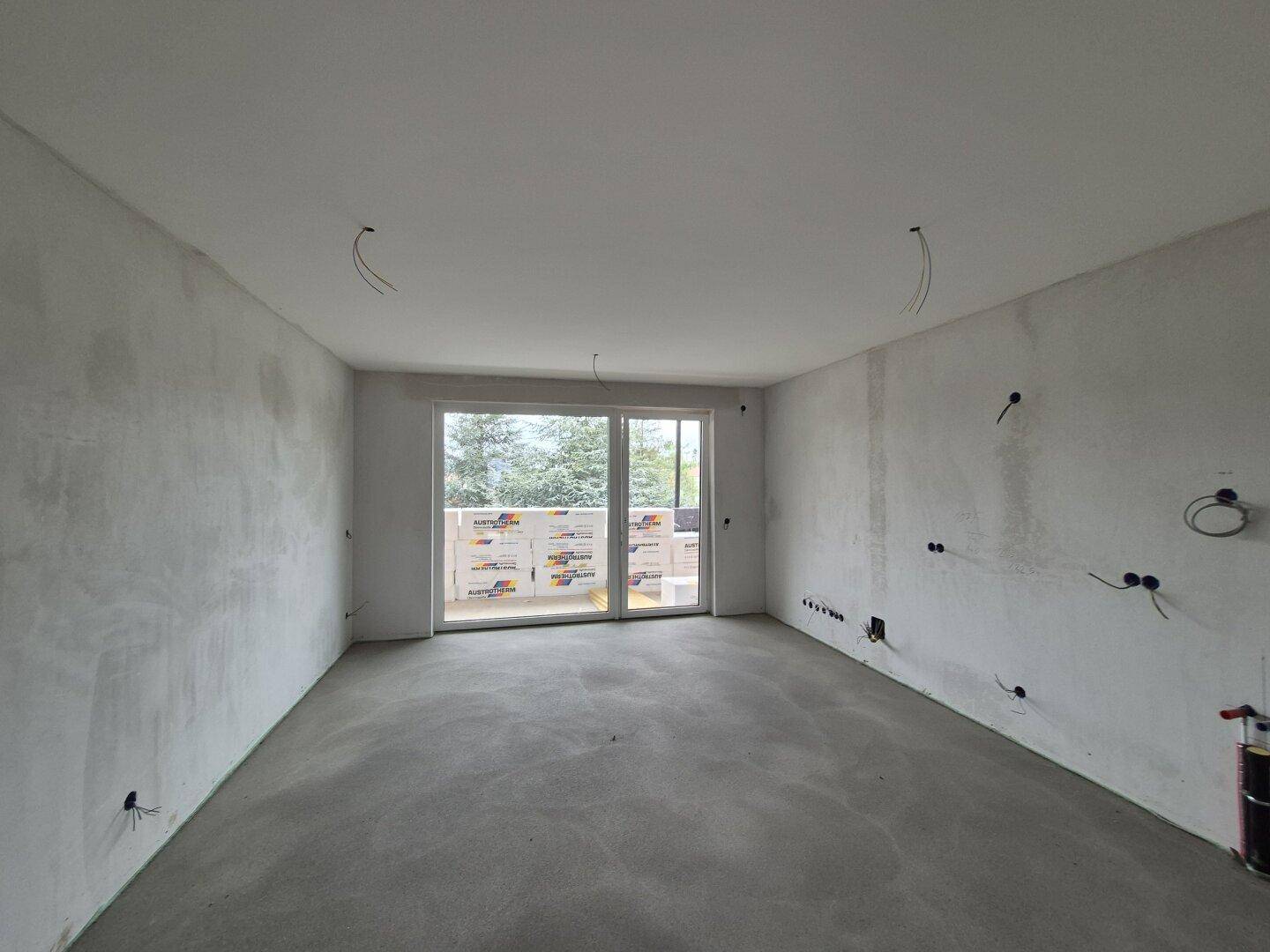 Rohbauzimmer mit Betonboden und vorbereiteten Elektroinstallationen, bereit für den Innenausbau.