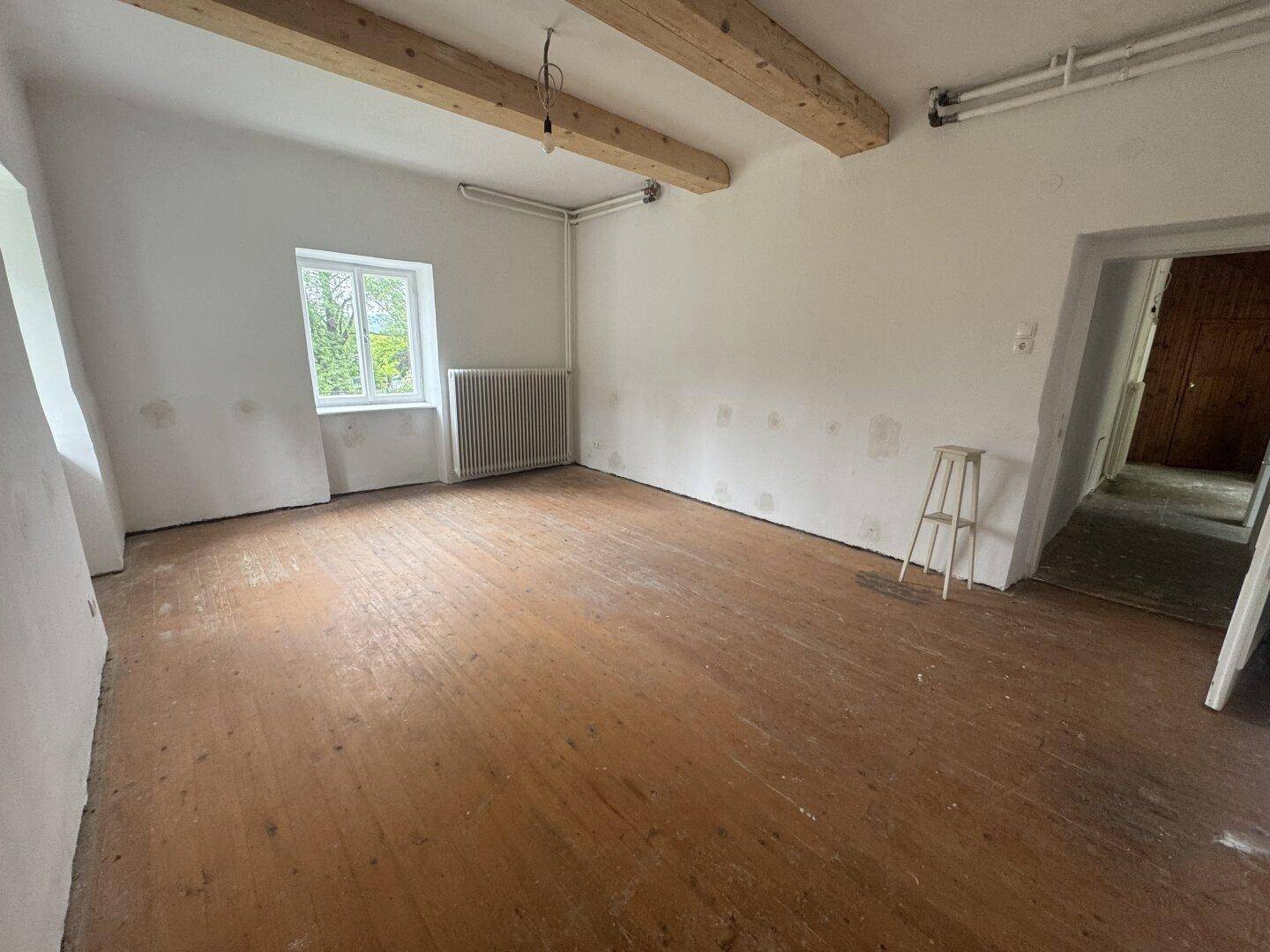 Geräumiger Raum mit Holzbalkendecke und Dielenboden, bereit für Renovierung.