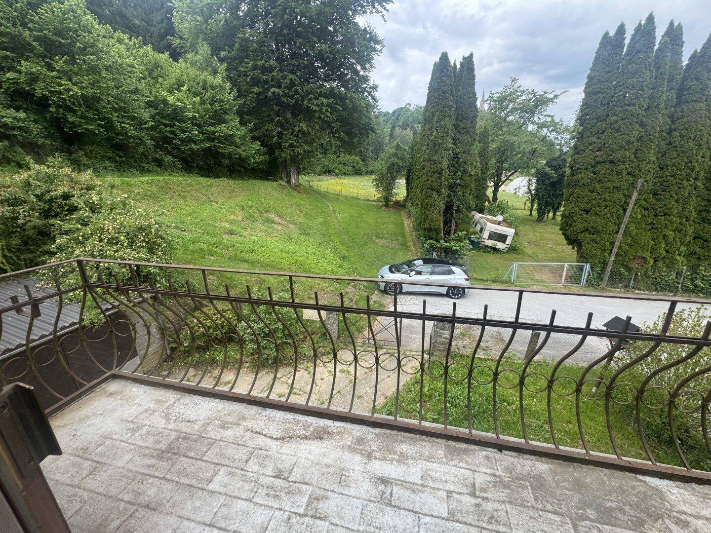 Balkon mit schmiedeeisernem Geländer und Blick auf die grüne Umgebung.