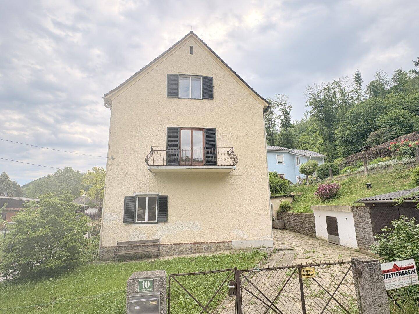 Vorderansicht des Hauses mit Balkon, Fensterläden und Zufahrt.