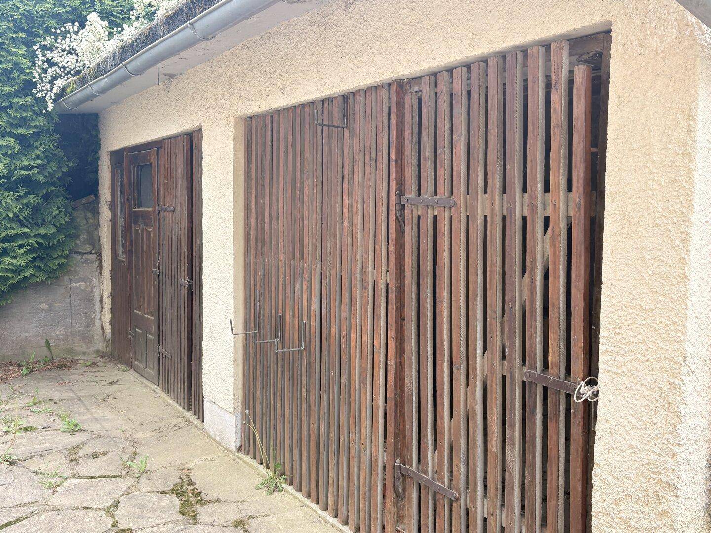 Zwei Garagentore aus Holz, die zu einem Nebengebäude führen.