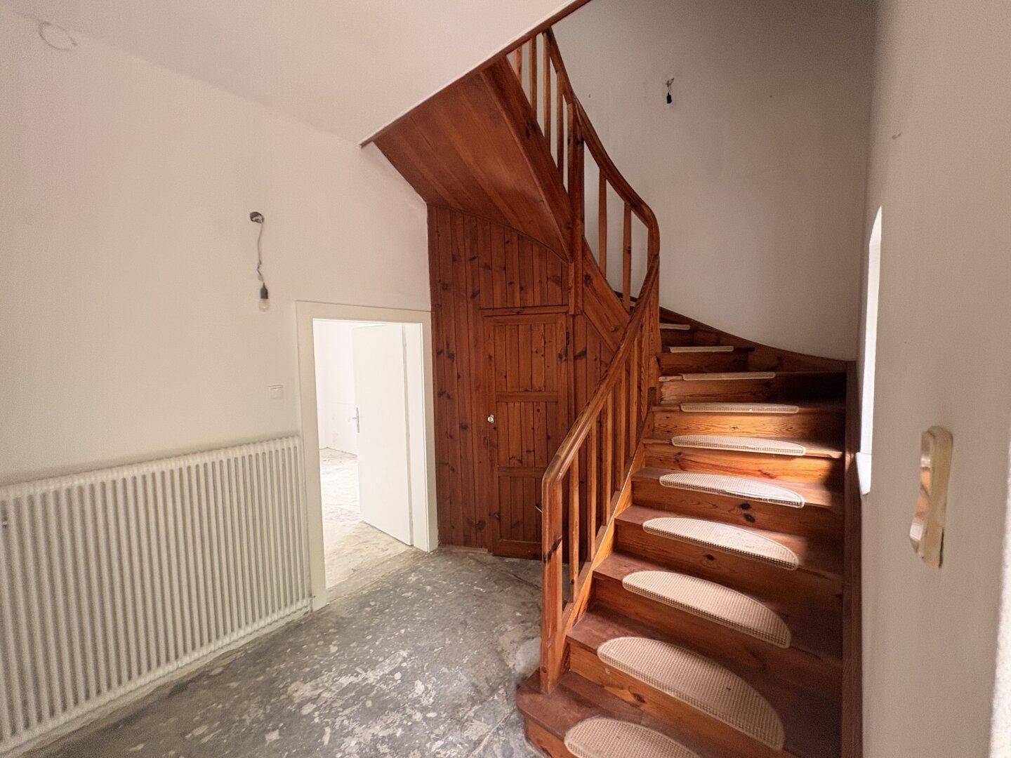 Holztreppe mit Geländer in einem Flur, der zu den oberen Etagen führt.