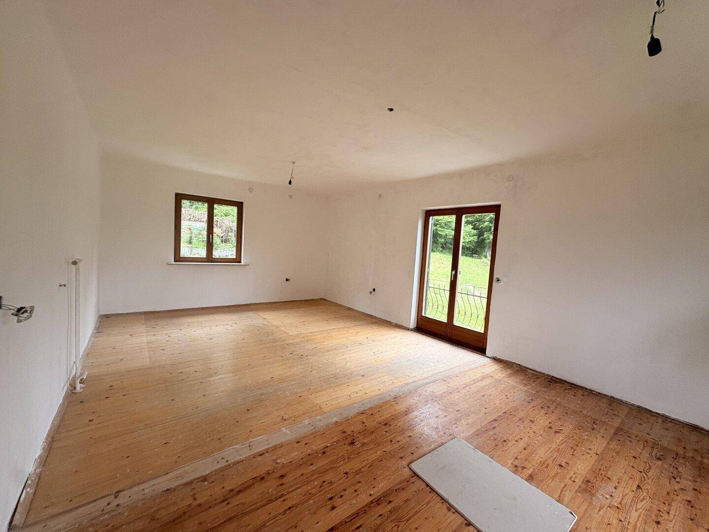 Geräumiger Wohnbereich mit Holzdielenboden und Zugang zum Garten oder Balkon.