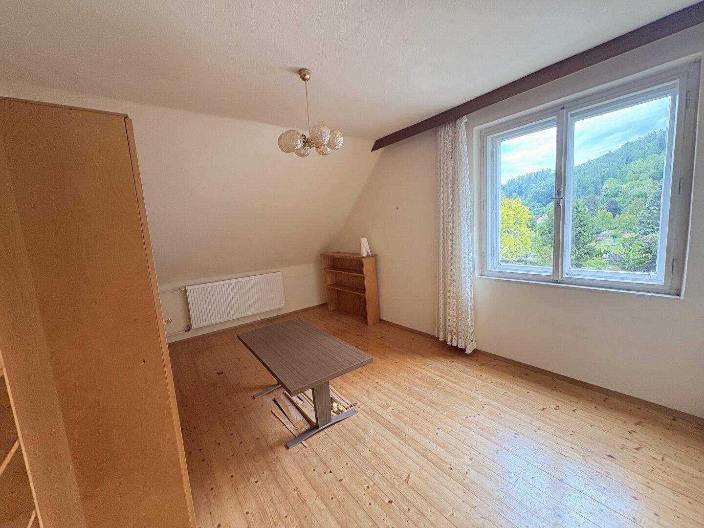 Dachgeschosszimmer mit Holzdielenboden, Schrägen und Fenster mit Weitblick.