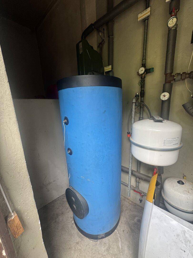 Blauer Warmwasserspeicher und weitere Installationen in einem Technikraum.