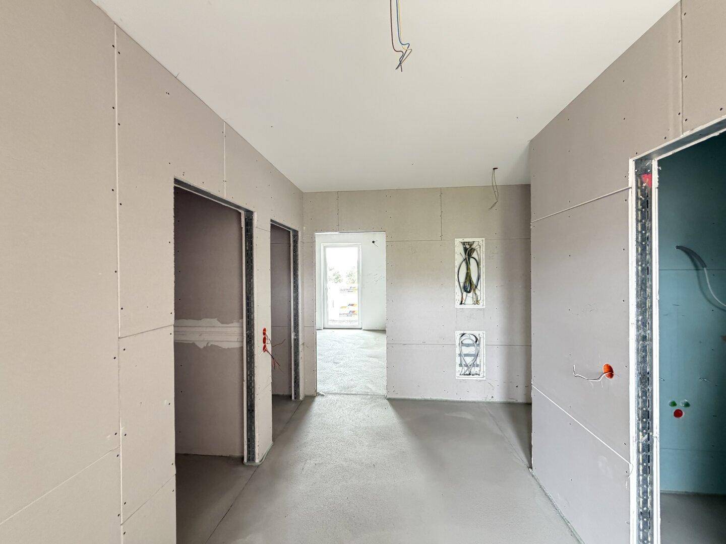 Flur im Rohbauzustand mit Trockenbauwänden und sichtbaren Elektroinstallationen.