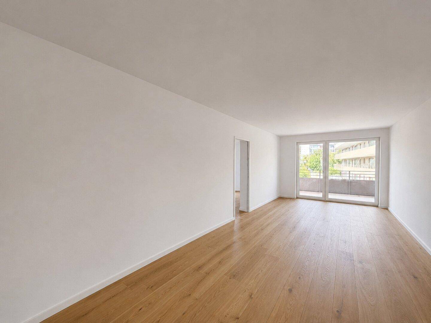 Helles, leeres Wohnzimmer mit neuem Holzboden und Zugang zum Balkon.