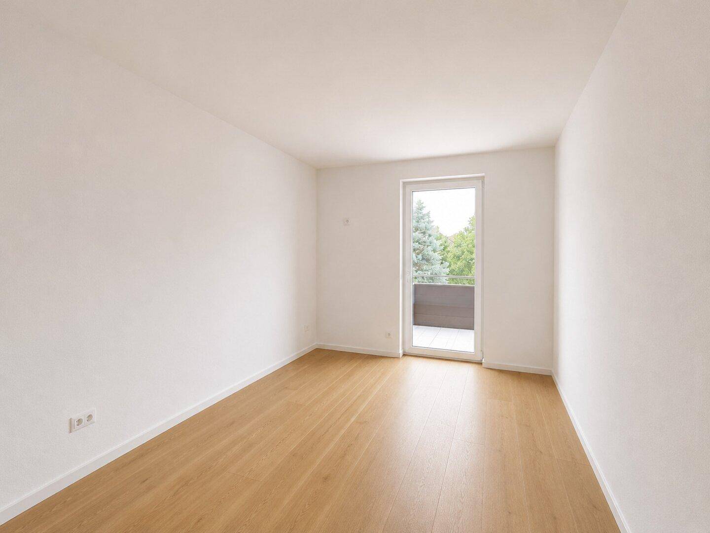 Leeres Zimmer mit hellem Holzboden und Zugang zu einem kleinen Balkon.