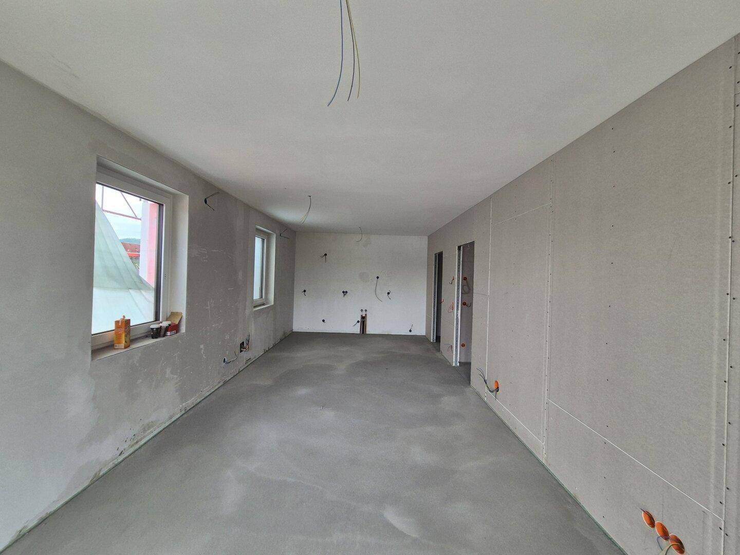 Unfertiger Innenraum im Rohbauzustand mit Betonboden und sichtbaren Installationen.
