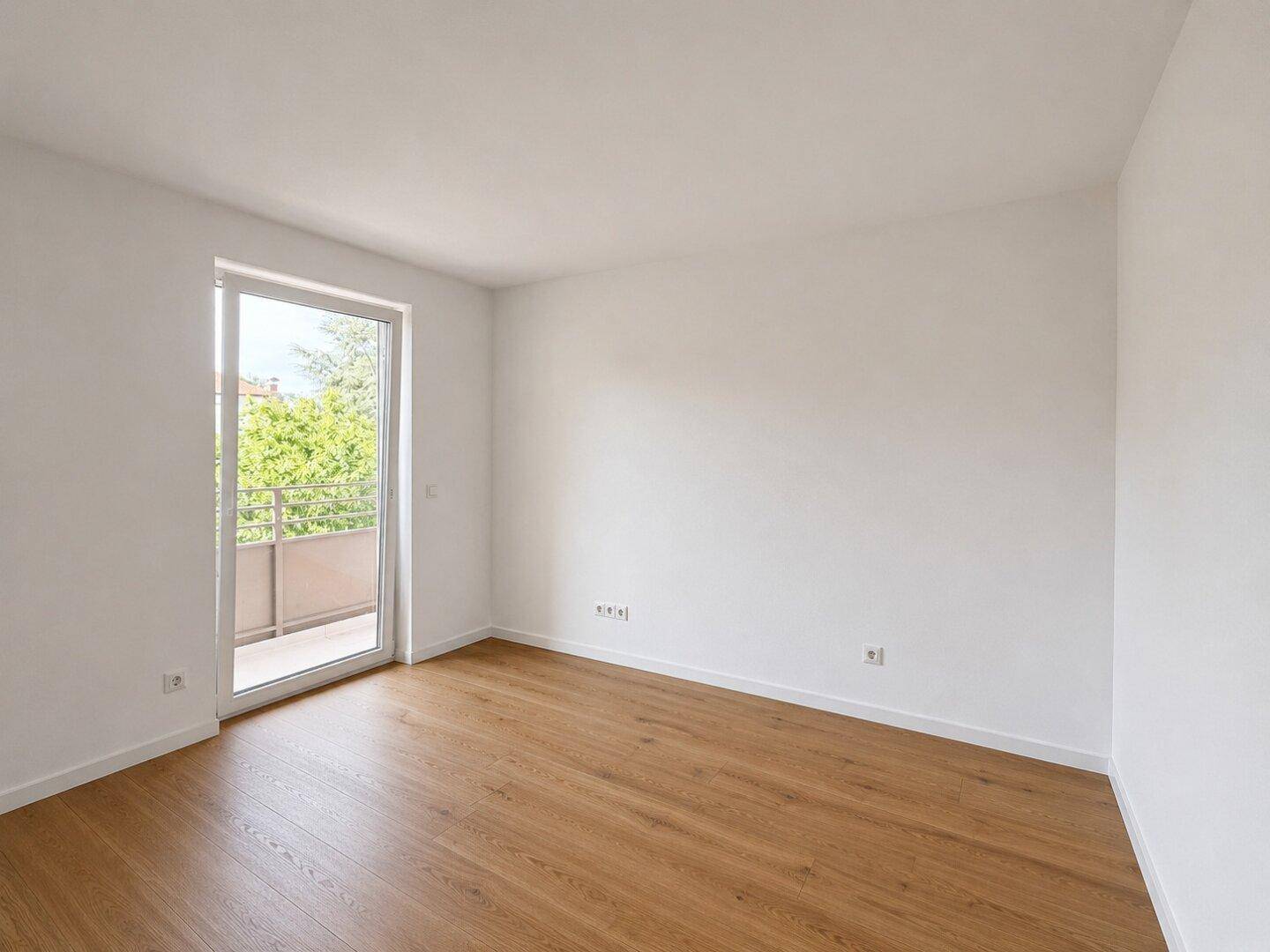 Lichtdurchfluteter Raum mit Holzboden und Zugang zu einem Balkon, ideal für Schlaf- oder Wohnbereich.