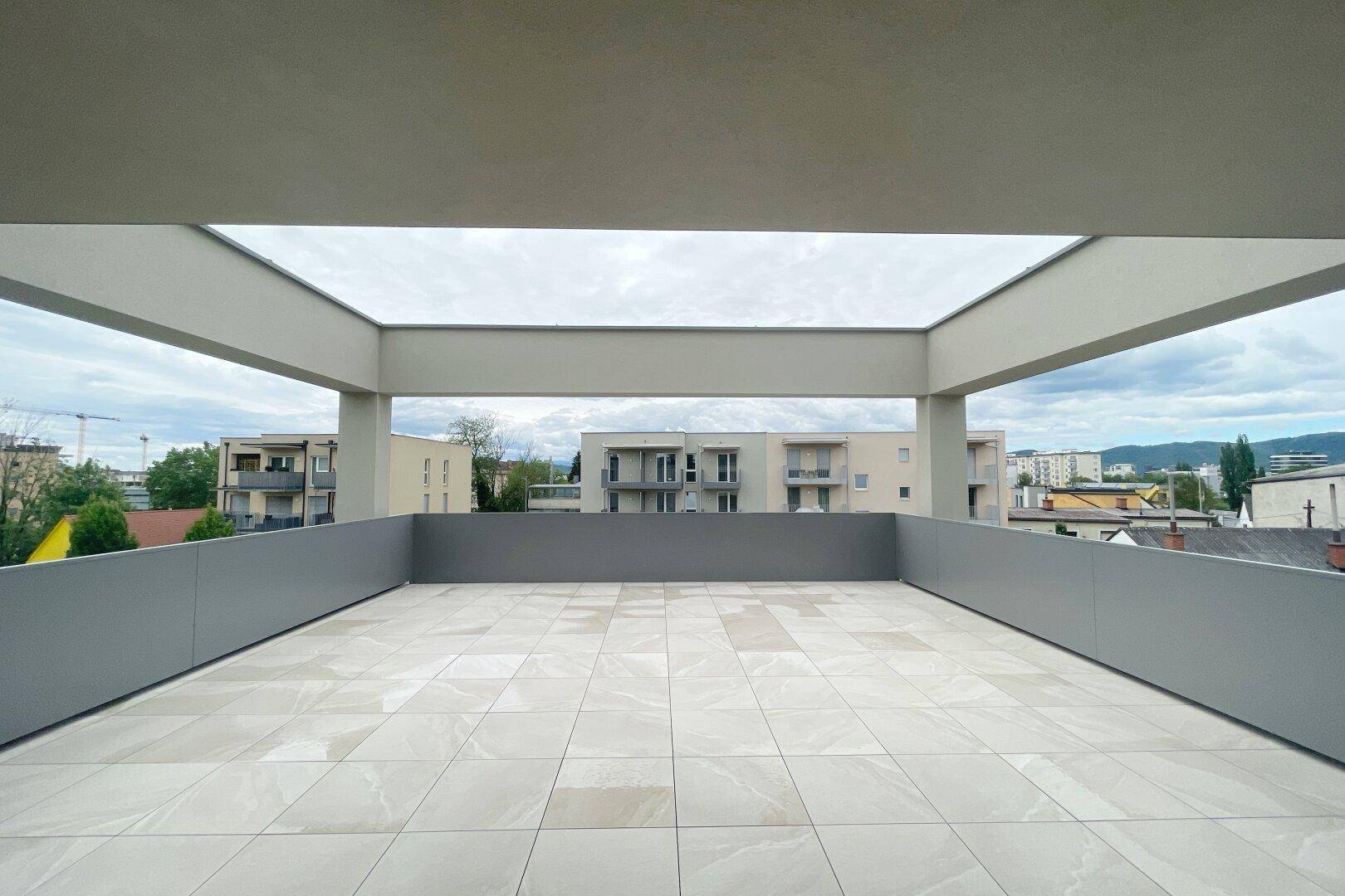Weitläufige Dachterrasse mit hellen Fliesen und moderner Architektur, umgeben von städtischer Bebauung.