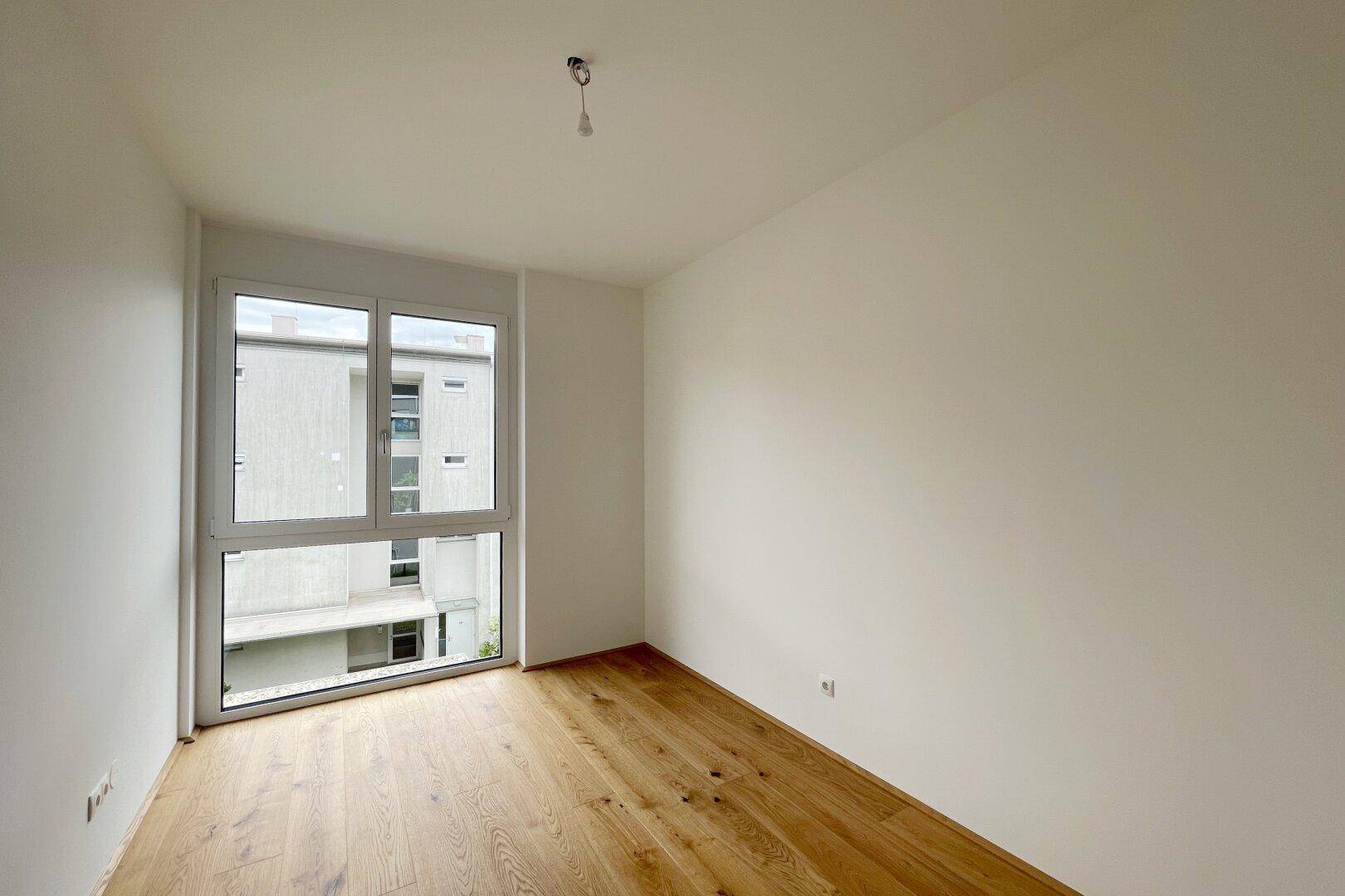 Helles Schlafzimmer mit Eichenparkett und großem Fenster, bereit für individuelle Gestaltung.