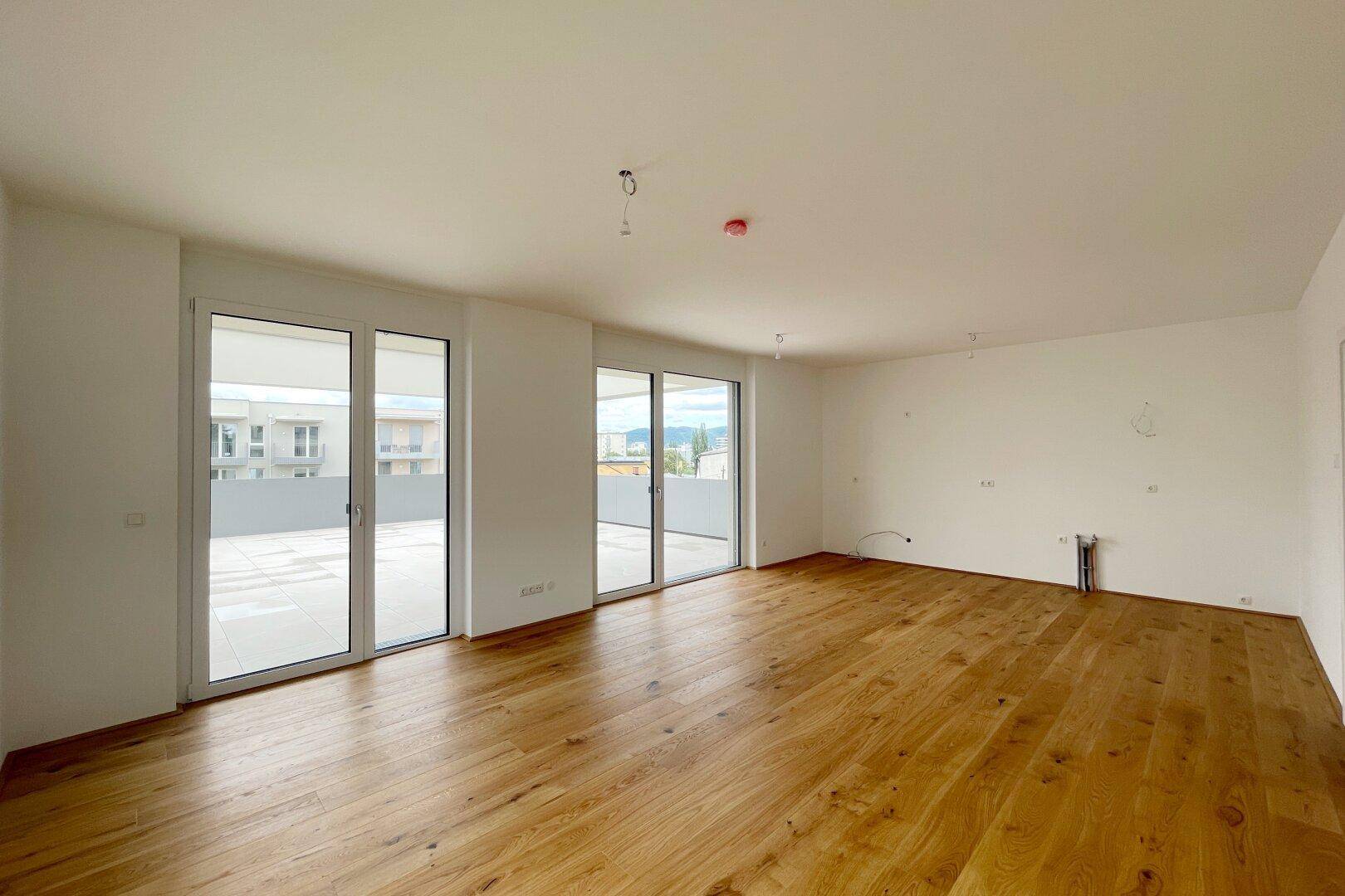 Heller, leerer Wohnraum mit hochwertigem Holzparkett und großen Glasfronten zur Terrasse.