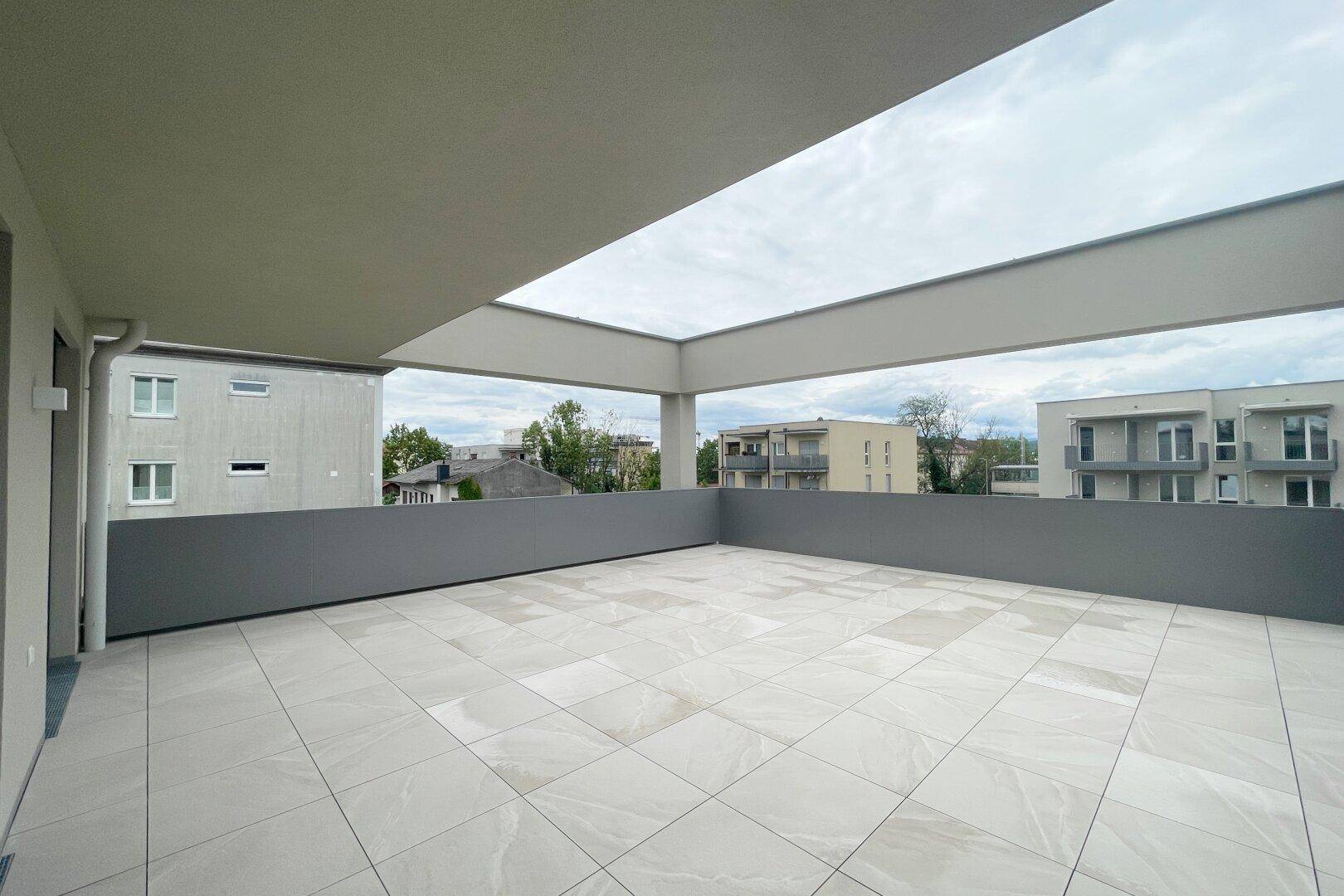 Moderne, weitläufige Terrasse mit hellen Bodenfliesen und Blick auf die umliegende Wohnbebauung.
