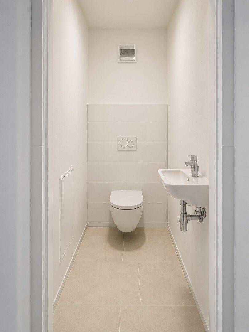 Modernes Gäste-WC mit wandhängender Toilette, kleinem Waschbecken und hellen Fliesen.