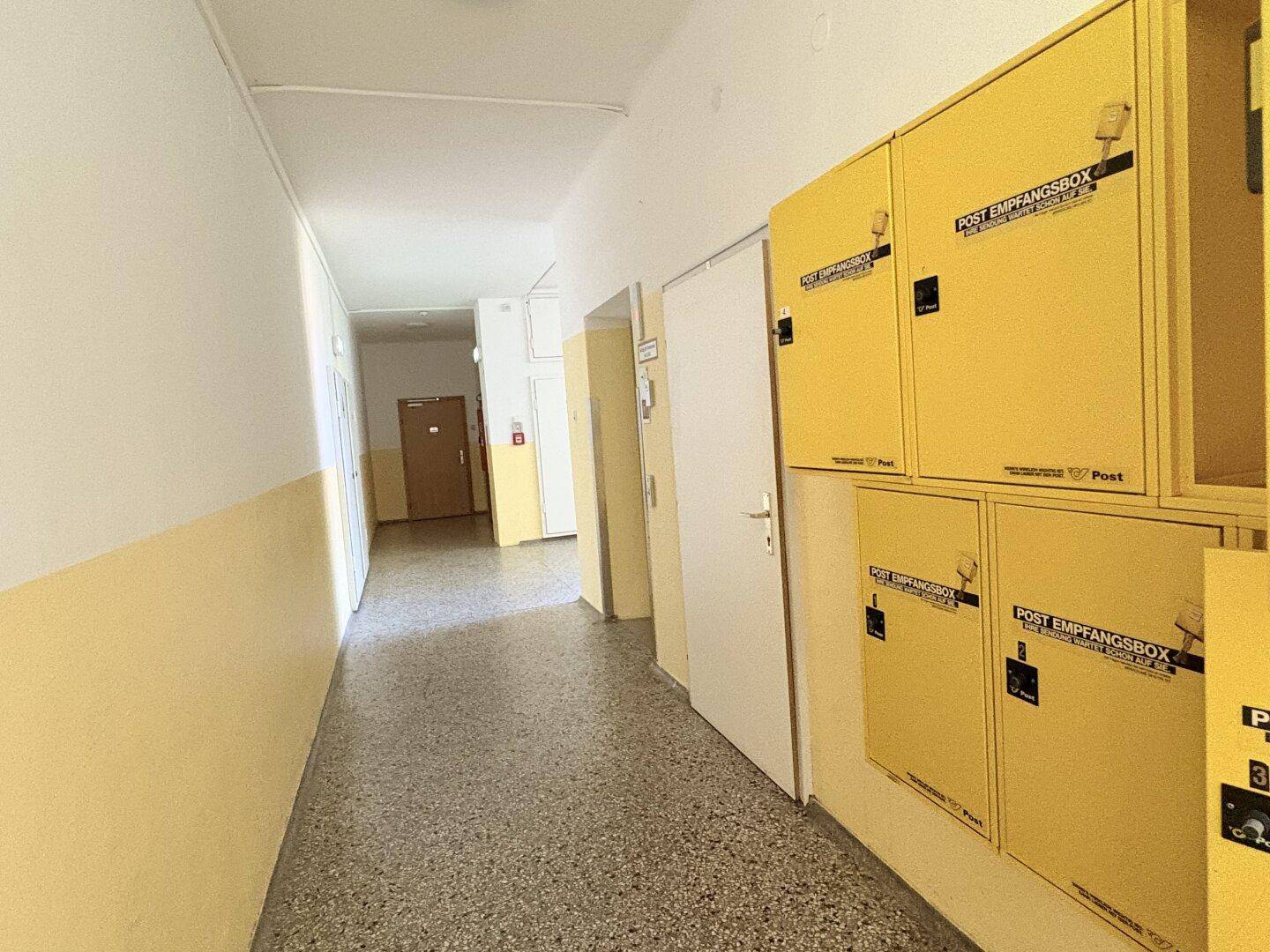 Langer Flur in einem Mehrfamilienhaus mit gelben Briefkästen und Zugangstüren.
