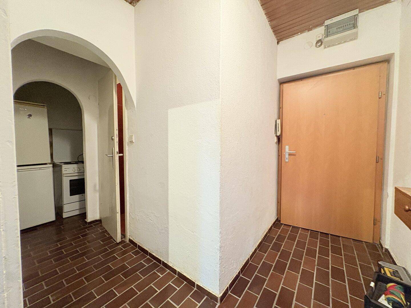 Flur mit braunem Fliesenboden und einem Durchgang zur Küche mit Kühlschrank.