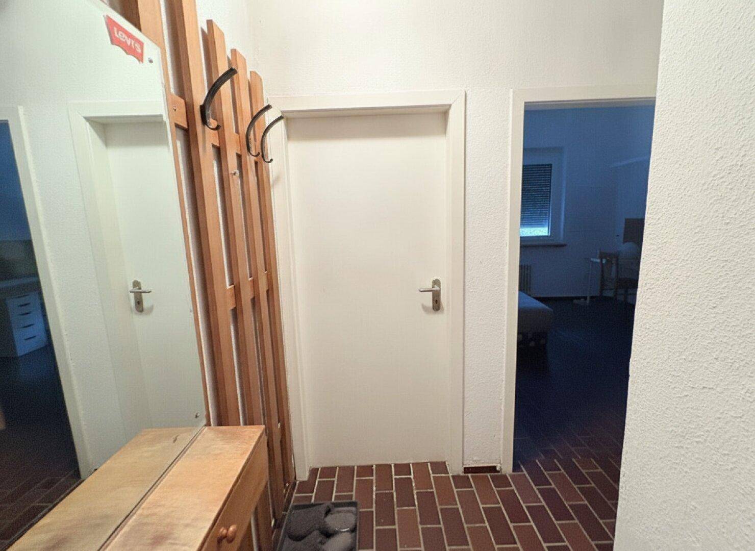 Eingangsbereich mit braunem Fliesenboden, Garderobe und Spiegel.