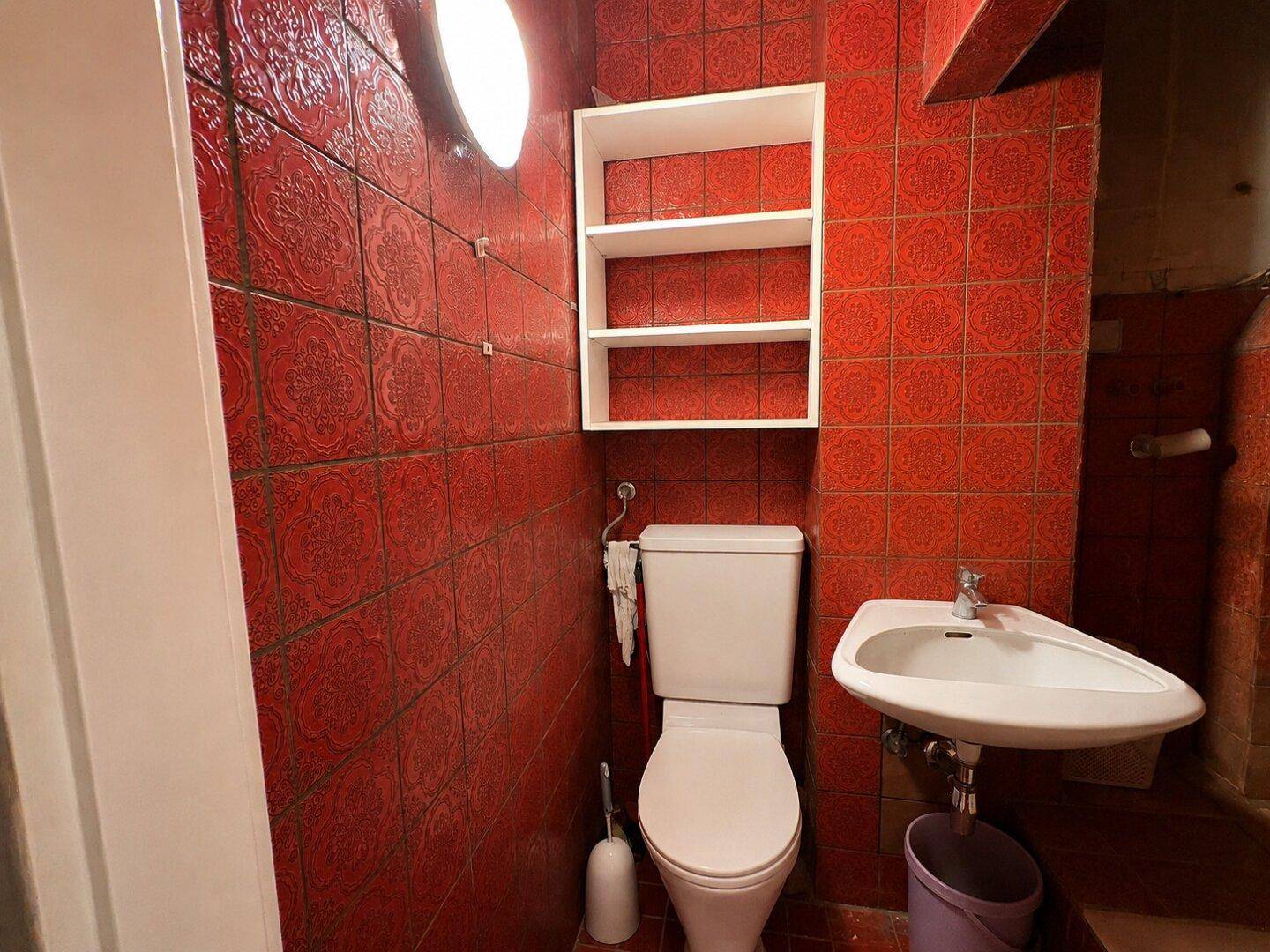 Kleines WC mit auffälligen roten Fliesen, Toilette und einem Eckwaschbecken.