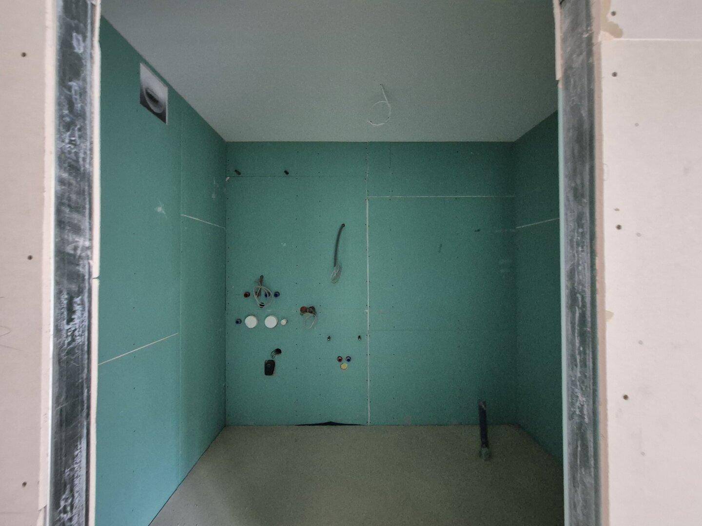 Badezimmer im Rohbau mit grünen Feuchtraumplatten, vorbereitet für die Installation der Sanitäranlagen.